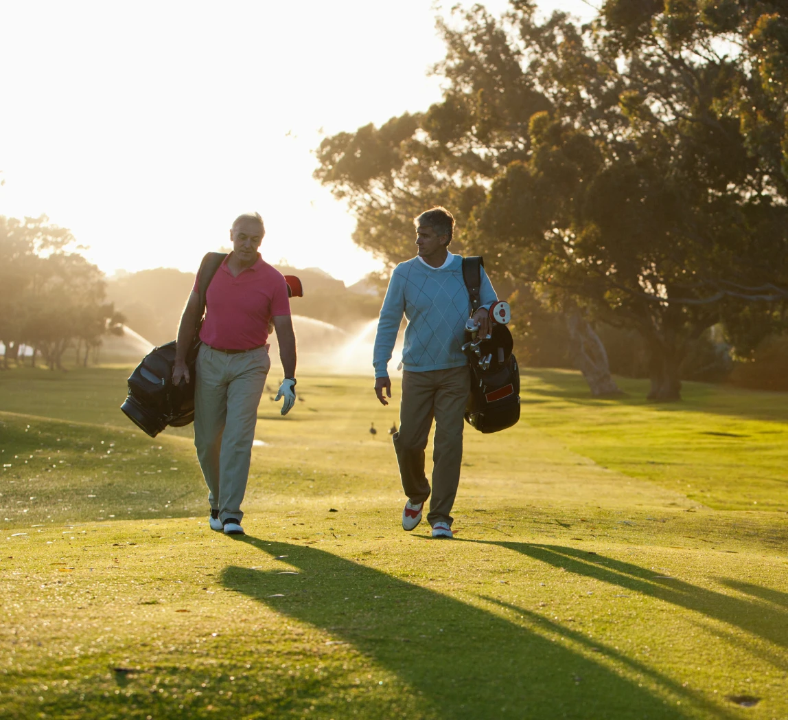 Golfers carrying bags at sunrise